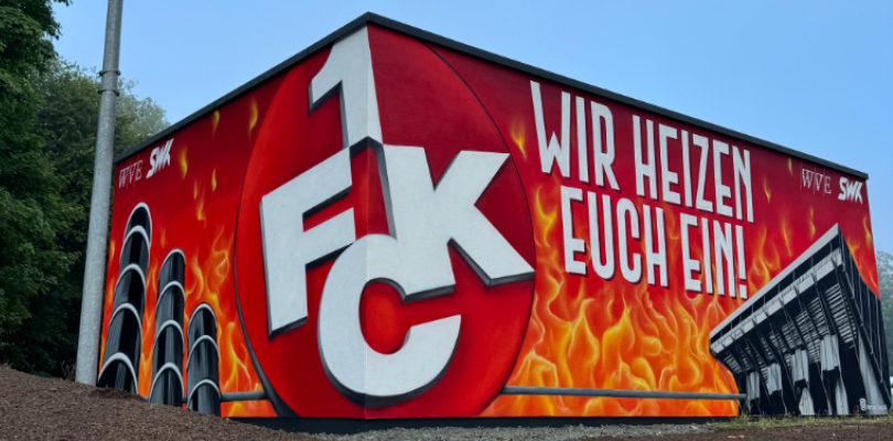 Fernwärmestation am Fritz-Walter-Stadion mit ganzflächigem Graffiti. Das Graffiti zeigt vor Flammenhintergrund die Wärmebehälter der SWK aud der Karcherstraße (3 Türme), das Logo des !. FC Kaiserslautern und die Außenansicht der Osttribüne.