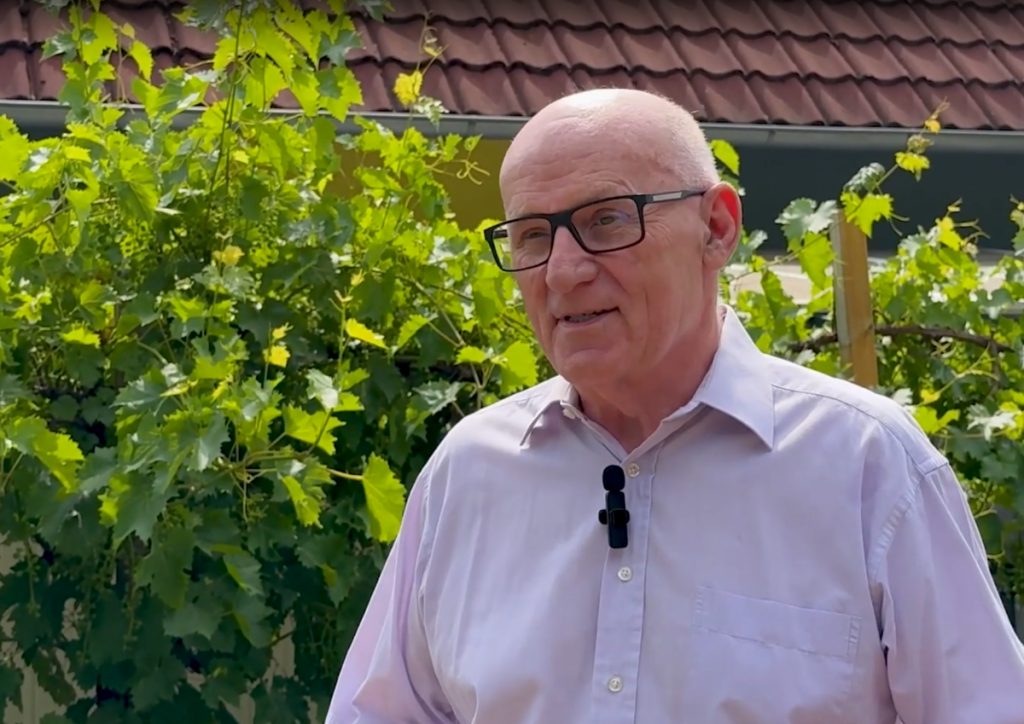 Der SWK-Solar-Kunde Manfred Schneider, steht in seinem sommerlichen Garten. Im Hintergrund ist das Dach des Eigenheims mit einer Photovoltaik-Anlage zu sehen.