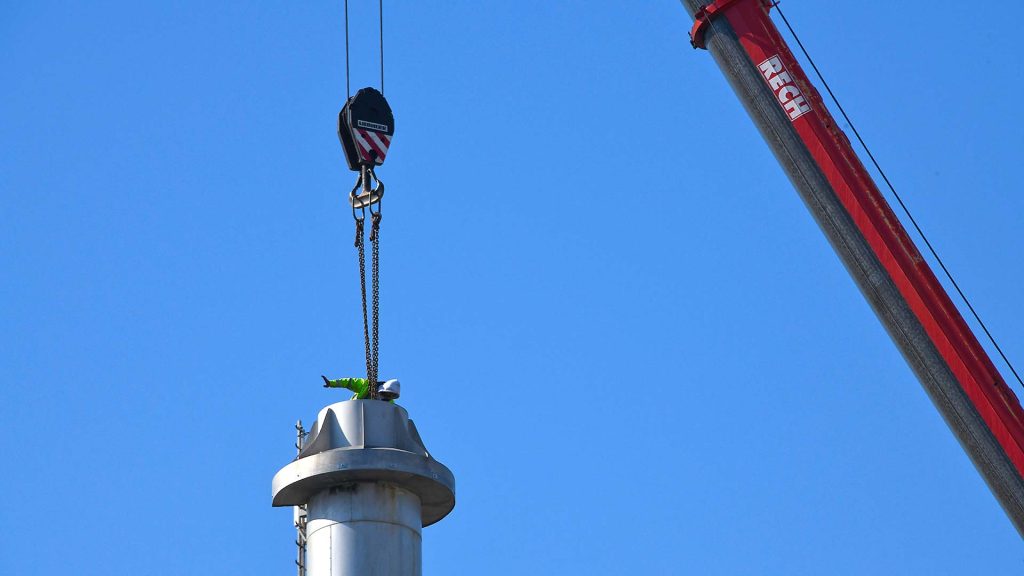 In luftiger H&ouml;he - selbtverst&auml;ndlich gesichert - gibt ein Abrissmonteur Anweisungen zur Fixierung f&uuml;r den Kranf&uuml;hrer und das Bodenpersonal.