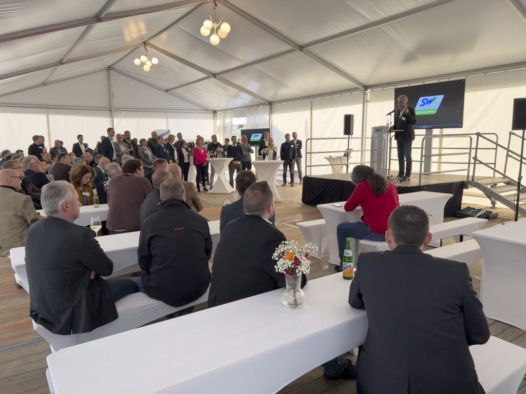 Dr. Weichel h&auml;lt eine Ansprache zur Er&ouml;ffnung der Veranstaltung. In einem Zelt sitzen und stehen ca. 50 Personen