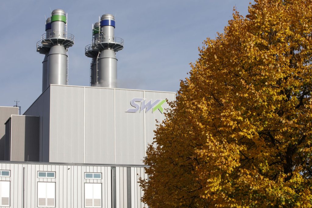 Hinter einem Baum mit goldbraunen Bl&auml;ttern sieht man im Hintergrund das Kraftwerk mit SWK Schriftzug