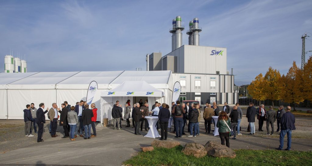 Ein Zelt steht auf dem Vorplatz des Kraftwerks. Vor ihm stehen Personen im Freien und an Stehtischen am Eingang des Zelts.