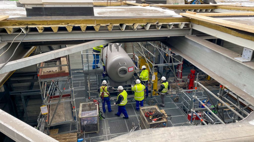 Mehrere Bauarbeiter bei der Montage einer Kesseltrommel im inneren des Kraftwerksgeb&auml;udes