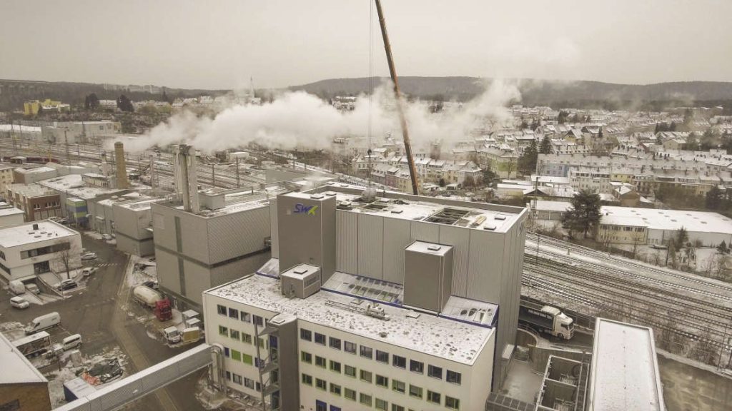 Dronenaufnahme von einem Kran, der eine Kesseltrommel durch das Dach ins Kraftwerk hebt