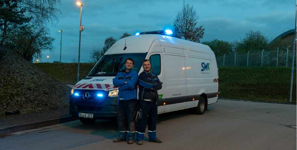 Imagemotiv der LAUTER LIEBE Kampagne. Es zeigt ein Werkstattfahrzeug der SWk (MErcedes Sprinter, das über Blaulicht verfügt. Vor dem Wagen stehen zwei SWK-Monteure, die freundlich in die Kamere lächeln.